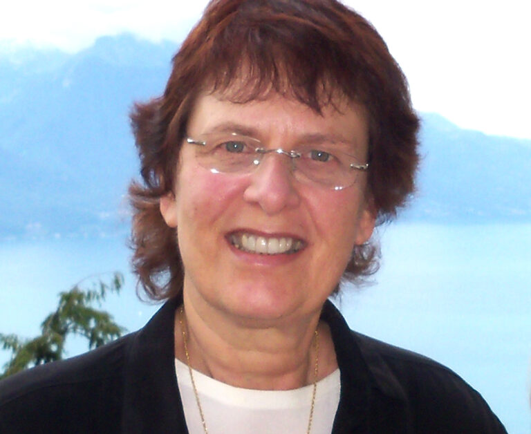 Dr. Francine Shapiro smiling outdoors with a lake and mountains behind her